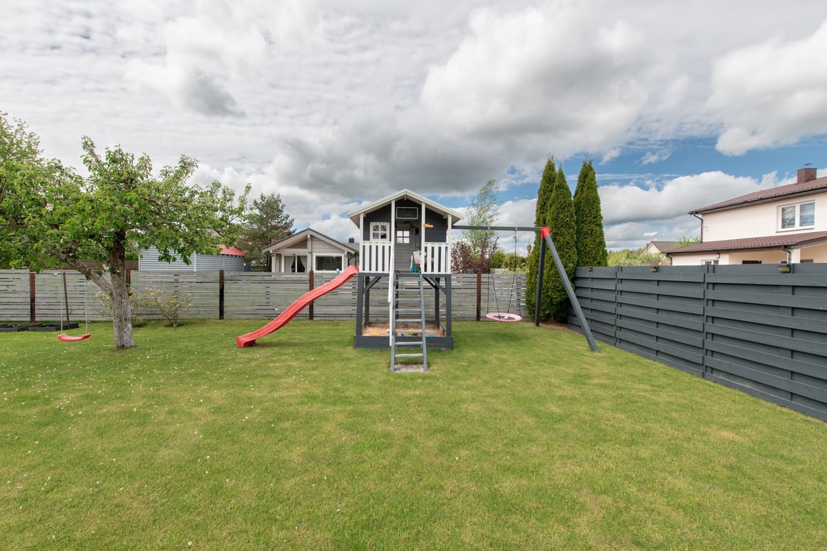 A playground with a slide and swings in a fenced garden