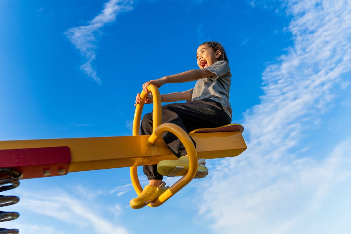 A happy young girl on a yellow seesaw at a playground