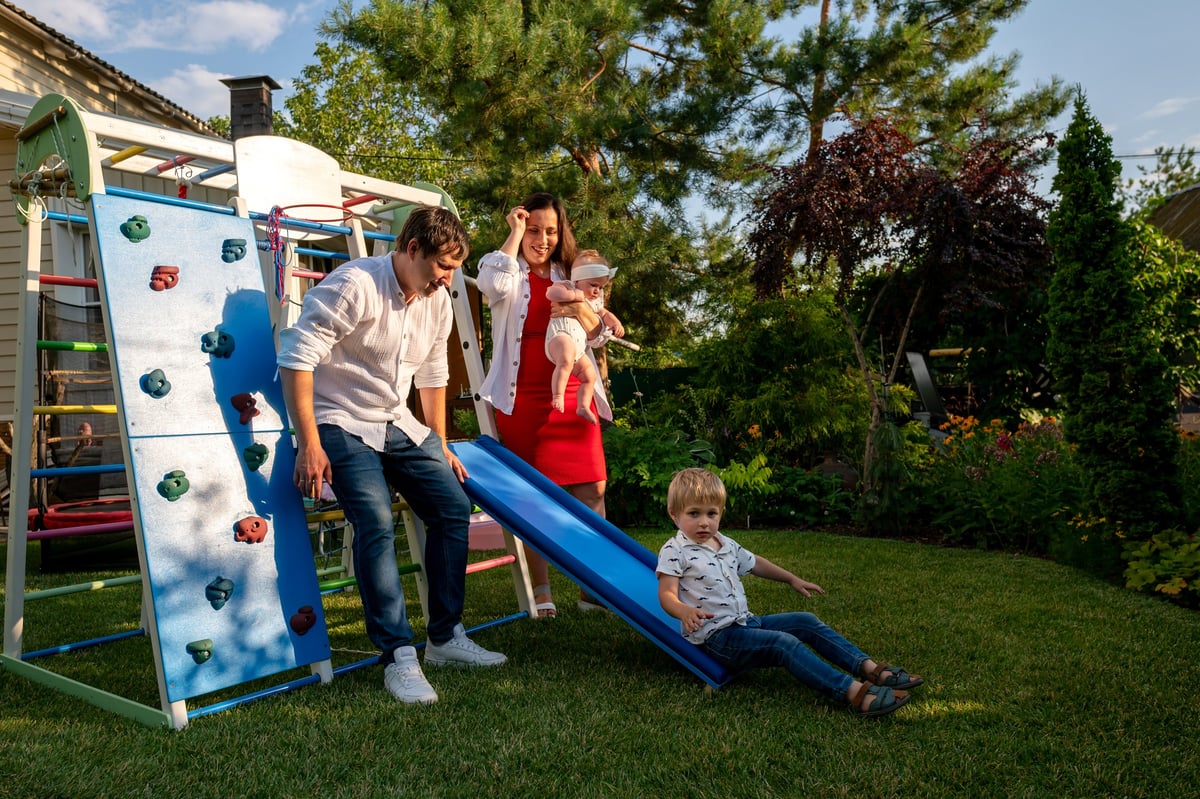 A child playing on a finished backyard playset while family supervises