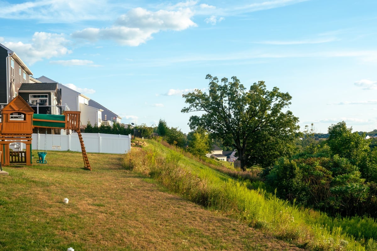 A backyard playground with a compact wooden playset beside a grassy hill