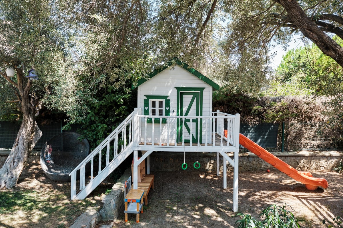 A children's playhouse with slide and gymnastic rings in a shaded garden