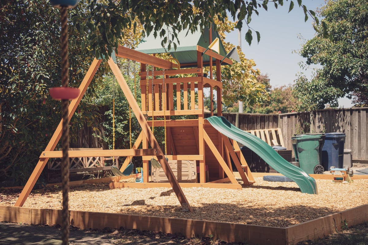A wooden playground with a slide and swings in a backyard